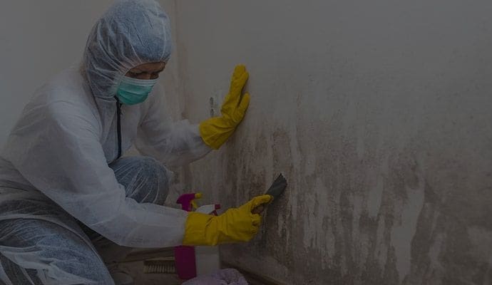 A person in a protective suit is cleaning a wall with a spatula.